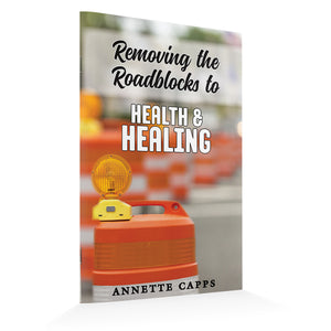 Book cover with construction barrier and warning light, titled 'Removing the Roadblocks to Health & Healing' by Annette Capps.